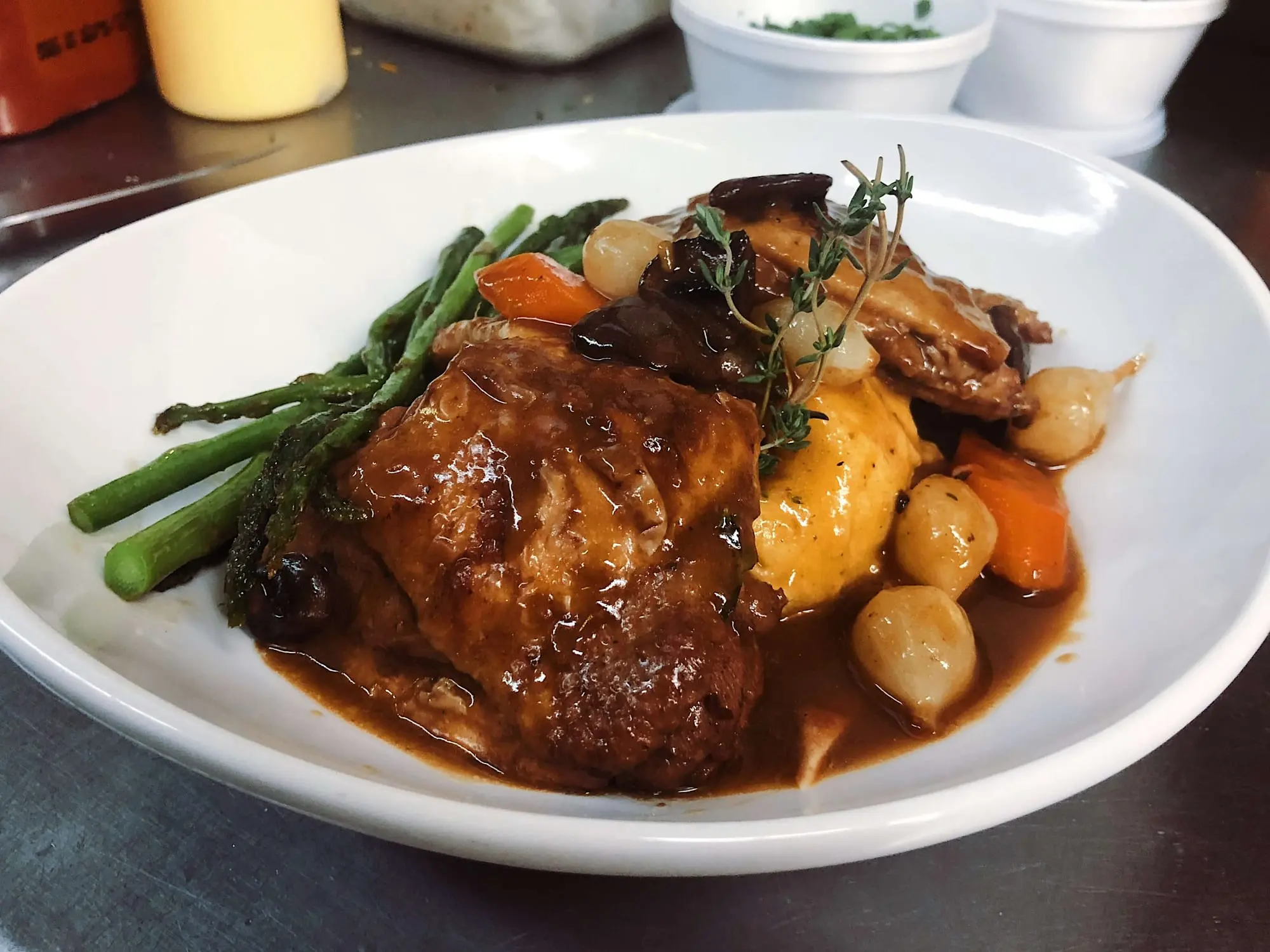 A plated entree in brown gravy with pearl onions, carrots and asparagus